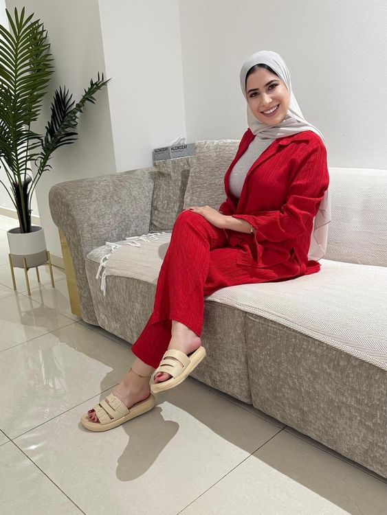 Woman in red outfit and beige slide sandals sitting on a sofa.