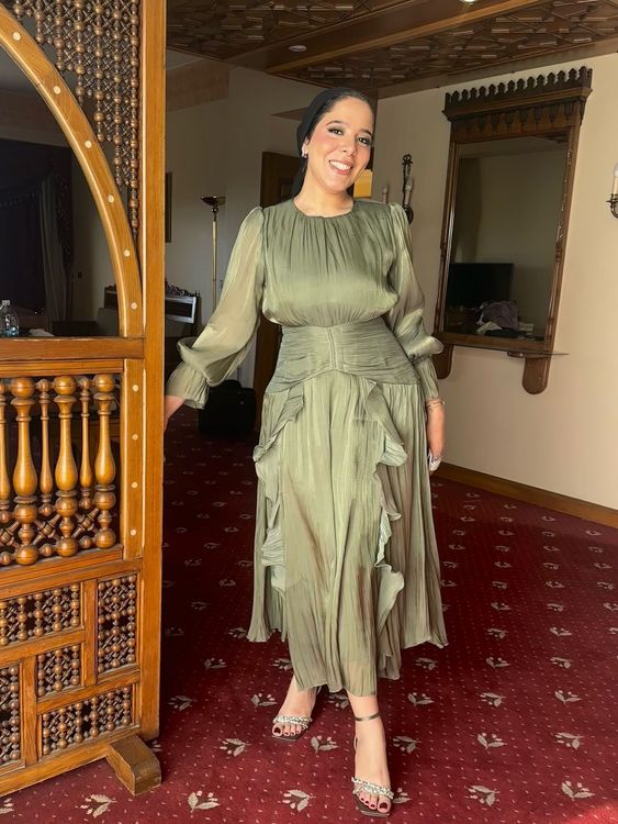 Woman in olive green layered dress and strappy heels in an elegant setting.