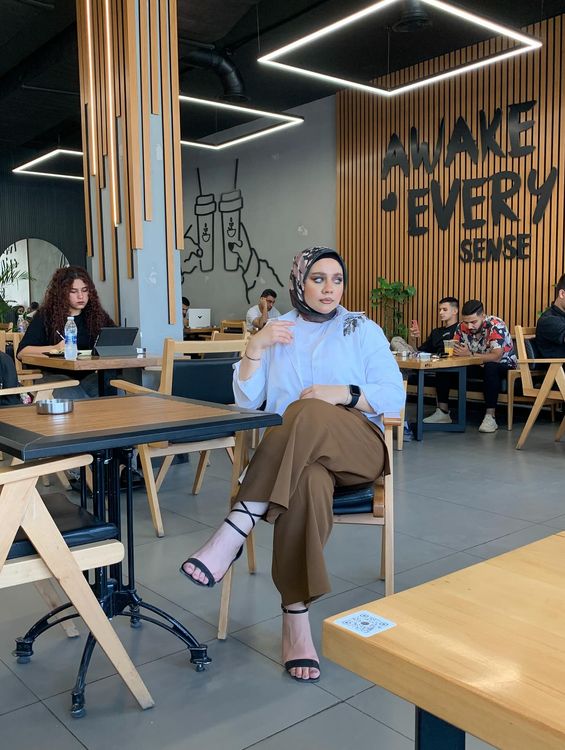 Woman in white blouse and brown trousers with strappy heels in a café.
