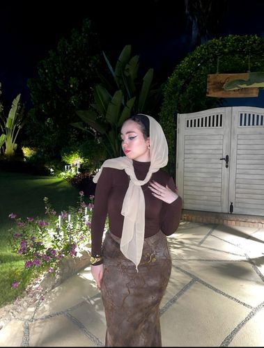 Girl in brown long-sleeve top and patterned skirt barefoot in garden setting.