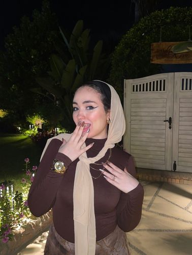 Woman in brown turtleneck and patterned skirt with hijab in garden setting