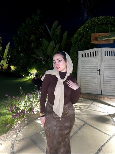 Ashrkat wearing a brown top and patterned skirt with a hijab in a garden setting.