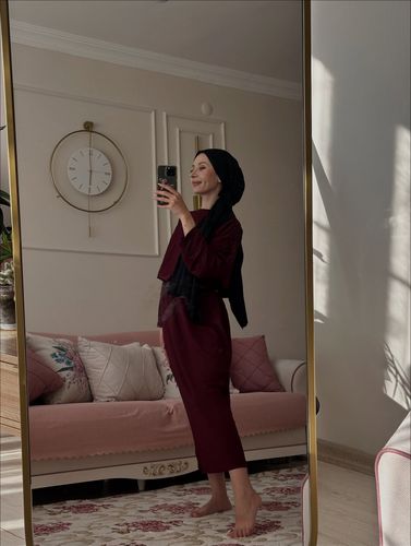 Woman in maroon loungewear and hijab in a cozy living room.