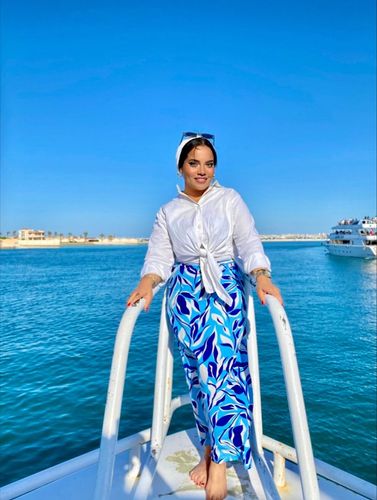 Girl in white top and blue patterned trousers barefoot on a boat.