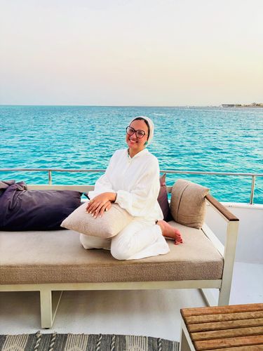Woman in white outfit and open-toe sandals sitting on a yacht.