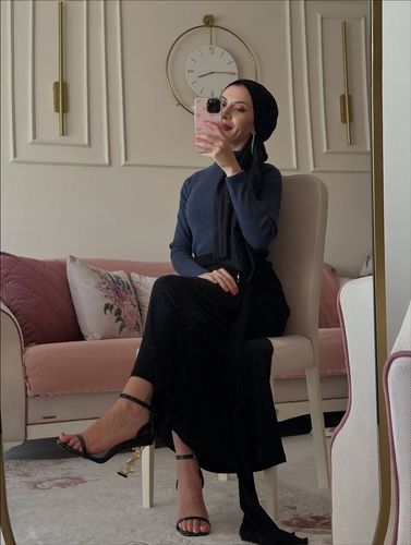 Woman in navy long-sleeved top, black skirt, and strappy heels in a stylish room.
