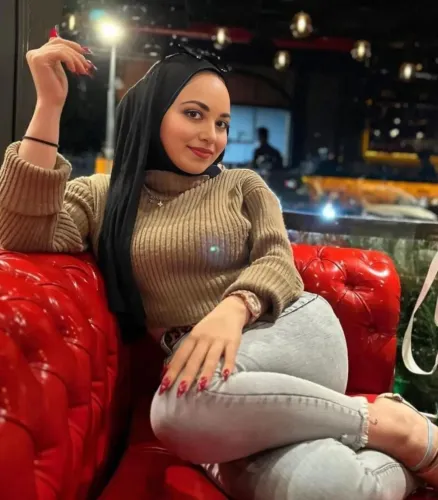 Girl in beige knit sweater and light-wash skinny jeans, barefoot in modern restaurant setting.