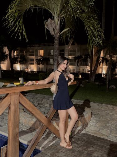 Young woman in a navy halter dress and tan flat sandals in an outdoor setting.