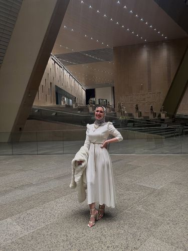 Woman in white dress and strappy heels inside a museum.