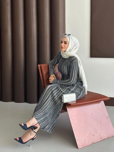 Woman in striped maxi dress and navy stilettos seated elegantly.