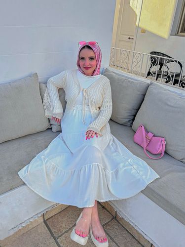 Woman in white dress and pink hijab sitting on a couch