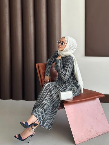Woman in striped dress and navy heels sitting on a modern chair.