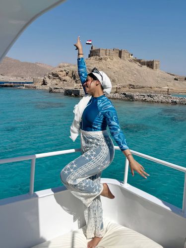 Rana Mahmoud in a patterned swim top and embroidered palazzo pants near turquoise waters.