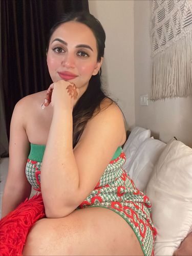 Woman in a colorful knit dress sitting on a bed.