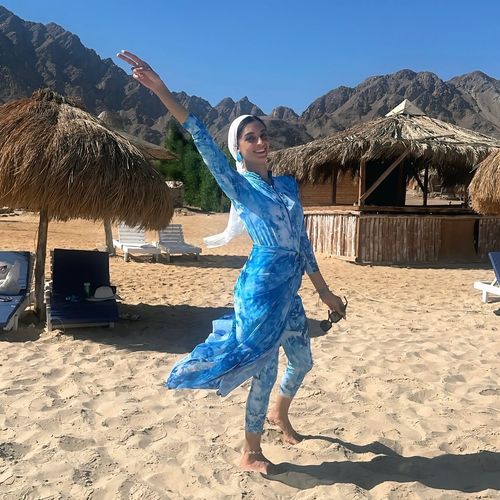 Woman in tie-dye dress and matching leggings barefoot on the beach.