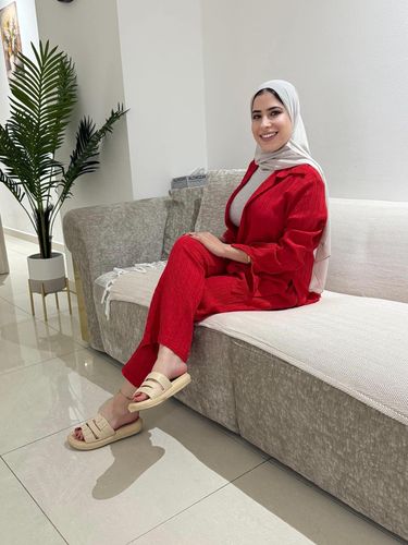 Woman in chic red outfit and cream slides sitting on a sofa indoors.