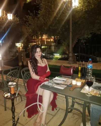 Woman in flowing red dress seated at an outdoor dining table.