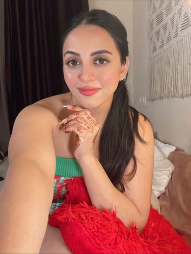 Woman in a floral green top with henna on her hand in a cozy setting