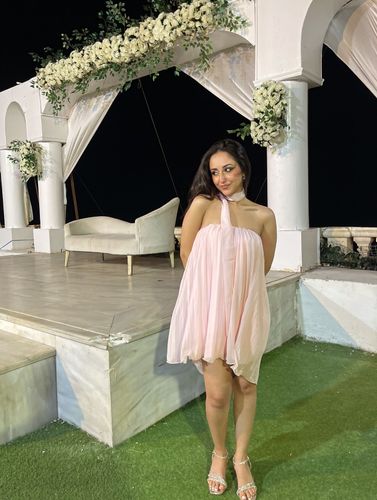 Woman in pastel pink dress and strappy sandals in an elegant outdoor setting.
