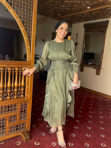 Woman in olive green dress and silver strappy heels in luxurious setting.