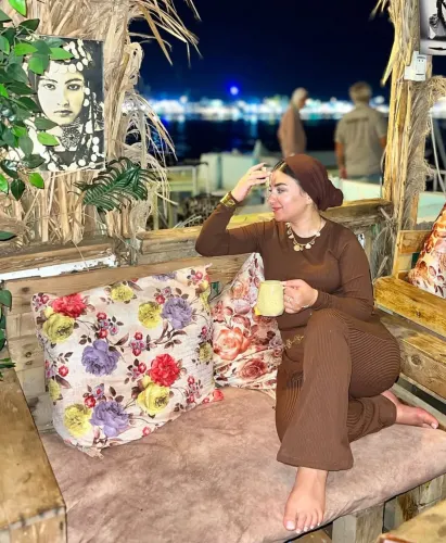 Woman in brown ribbed loungewear, barefoot, sitting on floral cushions with a cup in hand.