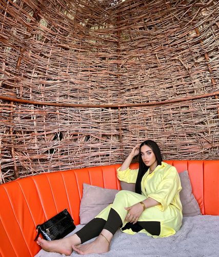 Girl in bright yellow oversized shirt and black leggings, barefoot in a woven setting.